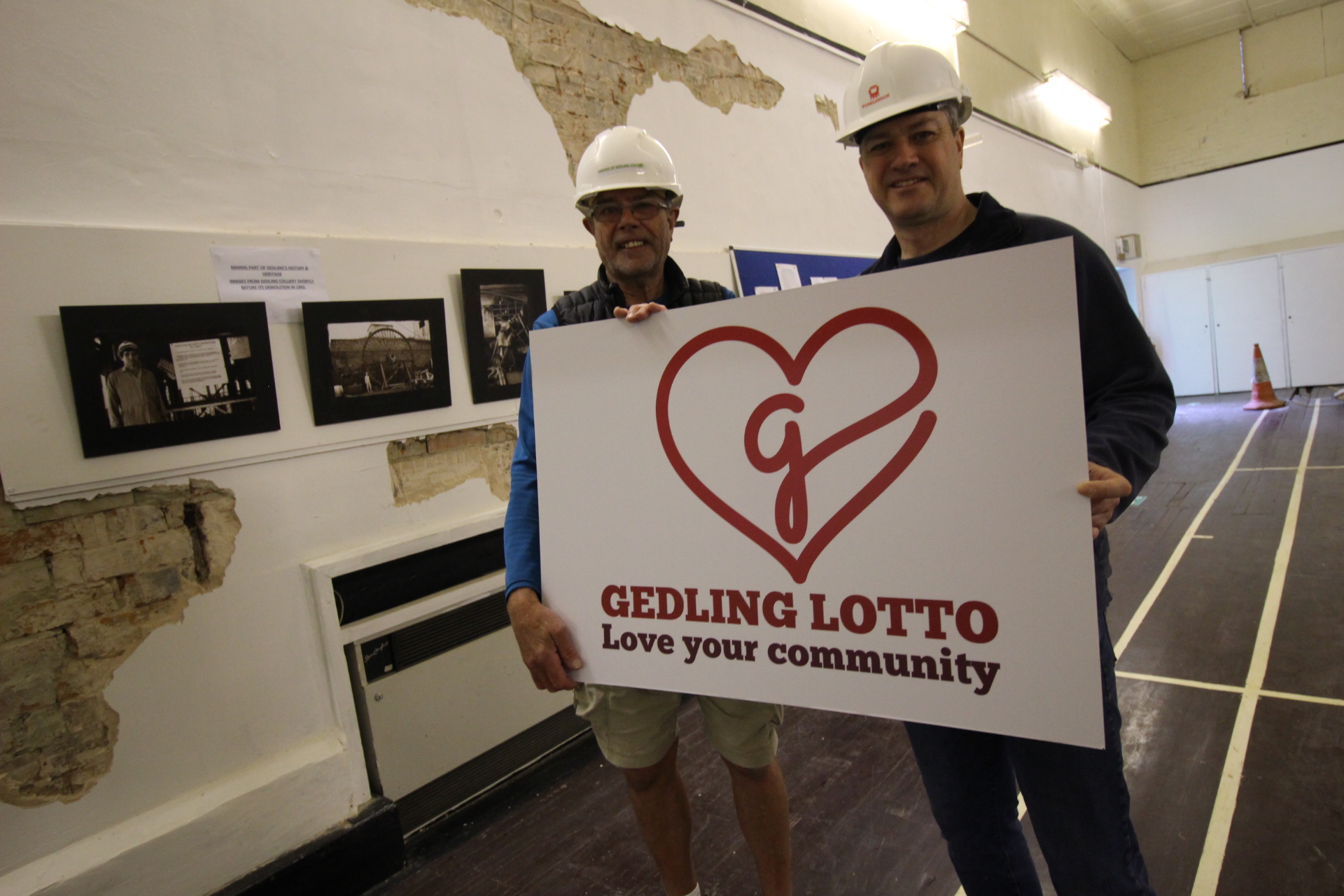 Two men with a lotto sign inside the youth club wearing hard hats